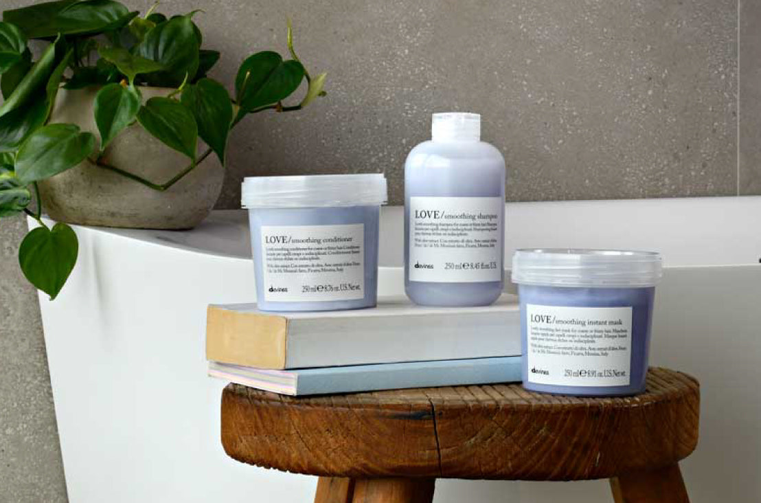Davines Love Smoothing Shampoo, Instant Mask, and Conditioner sitting on a wooden stool