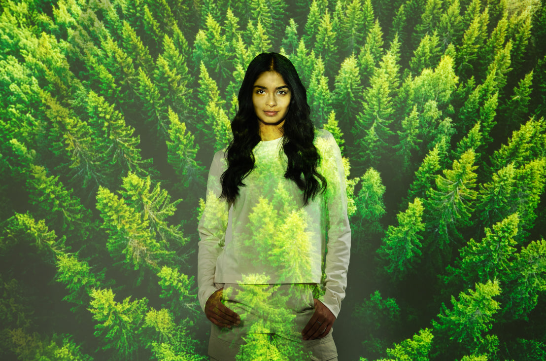 Woman with dark hair standing in front of an image of green forest trees