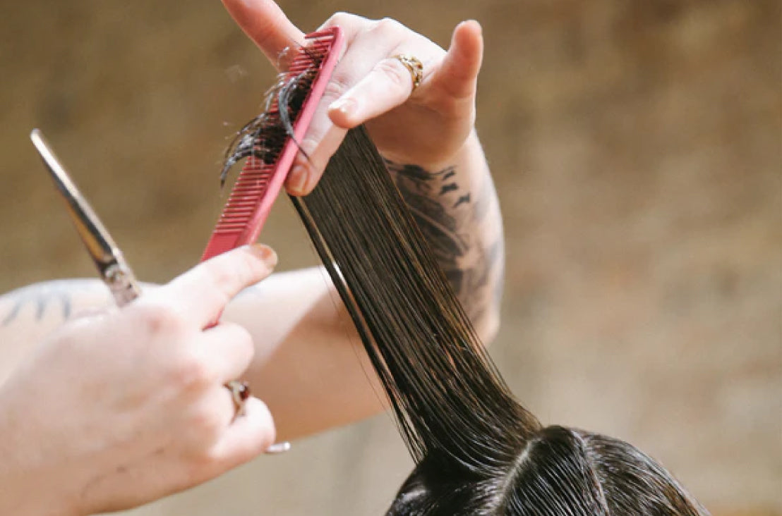 section of hair being cut by hands holding scissors and a pink comb